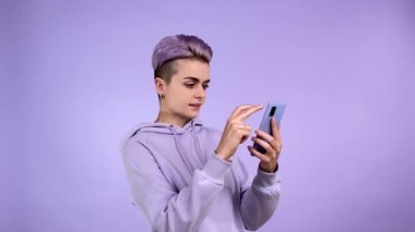 Mor kapüşonlu kapüşonlu, neşeli, genç bir kadın. Sosyal medya, tek renkli arka planda izole edilmiş internet sitesi. Mor saçlı, gülümseyen bayan hippi akıllı telefon kullanıyor.