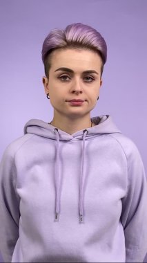 Modern yetişkin bir kadının menekşe rengi arka planda başını sağa sola çevirmesinin dikey görüntüsü. Mor kapüşonlu modaya uygun kadın özgünlüğü anlaşmazlığı ifade ediyor, kapalı alanda reddediliyor.