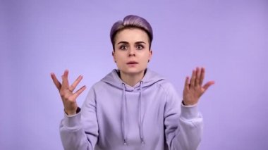 Kısa boyalı saçlı, hırslı, azarlayan, sert ifadeli, mor kapüşonlu bir kadın. Mor arka planda kapalı stüdyo çekimleri