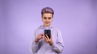 Neşeli, genç, genç, trend bir kadın. Havalı görünüm, akıllı telefon, en iyi teklif edilen fiyatı bulmak şaşırtıcı. Kapalı alanda mor arka planda izole edilmiş yeşil renkli cihaz ekranı gösteriliyor.