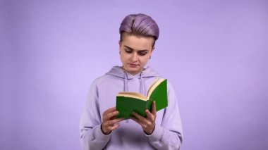 Mor arka planda izole edilmiş yeşil kapaklı, modaya uygun kısa saç stili kitap okuyan modern bir genç kadın. Kitabın sayfalarını çeviren üniversiteli bir bayan. Stüdyoda öykü yazma konusunda tutkulu.