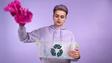 Geri dönüşüm işaretli kısa saçlı, kendine güveni olan Z jenerasyonu geri dönüşüm kutusuna plastik çöp atıyor ve mor arka planda nasıl izole edildiğini gösteriyor.