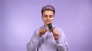 Büyüleyici genç yetişkin kadın nesli Z, modaya uygun görünümlü, klasik kaset tutan, kalemle sesli kaset çeviren, kapalı alanda mor arka planda izole edilmiş gülümseyen kameraya bakan. Sentetik dalga