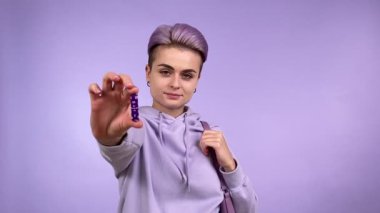 Kısa boyalı saçlı, kendine güvenen genç bir kadın tamponu kameraya yaklaştırıyor, çantaya kadın hijyen ürünlerini koyuyor, kapalı alanda nasıl izole edildiğini gösteriyor. Tek renkli konsept