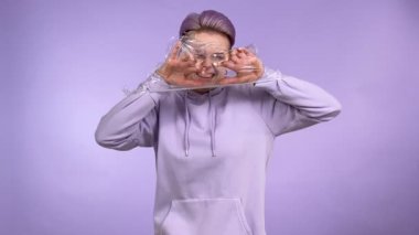 Genç yetişkin kadın nesli Z, sentetik ambalajla sarılmış, plastik malzemeyi yırtıyor, serbest kalıyor, kameraya bakıyor, derin bir nefes alıyor. Mor arka planda izole edilmiş kapalı stüdyo çekimi