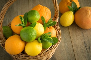 Hasır sepet dolusu narenciye meyvesi ahşap masanın üzerinde sağlam meyvelerin karşısında duruyor. Olgun limon, limon, portakal, nane yaprağı. Yaz taze hasat