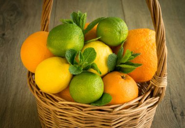 Tahta masada duran turunçgillerle dolu hasır el sepetinin yakın görüntüsü. Olgun limon, limon, portakal, nane yaprağı. Yaz taze hasat. Olgun tropikal meyvelerle dolu bir sepet.