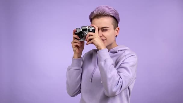 一个积极的年轻女性用老式的电影摄影机拍照 问Sb移动一点点 使用在紫色背景上隔离的复古风格设备生成Z 合成波概念 — 图库视频影像