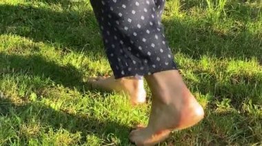 Güneşli yaz sabahında taze, yeşil çimlerde yürüyen kadın bacaklarının yakın görüntüsü. Genç yetişkin bir kadın gün doğumunda bahçede huzurun tadını çıkarıyor. Huzurlu bir an. Sağlıklı bir yaşam tarzı. Çekim