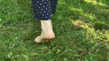 Güneşin doğuşuyla birlikte yeşil çimlerde gezinen kadın bacaklarının arka görüntüsü. Çıplak ayaklı kadın bahçede çim yürüyerek sabah tazeliğinin tadını çıkarıyor. Rahatlama, sağlıklı yaşam tarzı konsepti