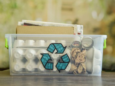 Arkaplanı bulanık ahşap masanın üzerinde çöp kağıdı dolu geri dönüşüm levhası olan şeffaf plastik bir kap. Eski kağıt ürünlerinin geri dönüşümü tekrar kullanılacak. Çevre koruma. Atık kağıt sıralama