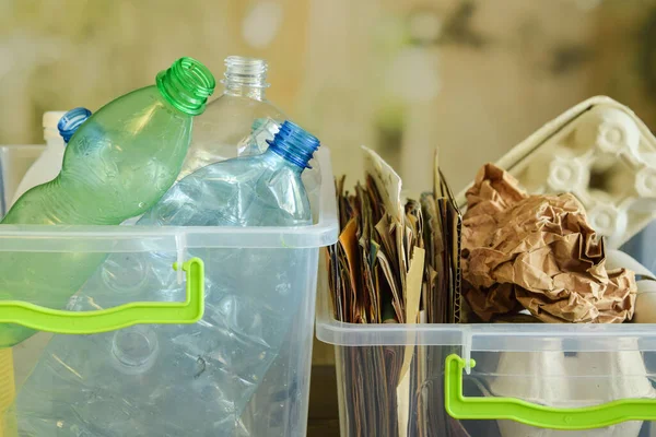 Two containers filled with multicolored plastic bottles and wastepaper on blurred background. Collecting plastic, paper for recycling, upcycling, downcycling. Environment conservation. Reducing waste