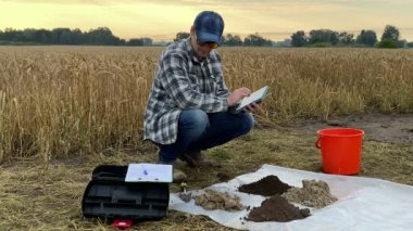 Agricultural scientist using tablet, entering data looking at sampling information sheet during soil testing at dawn outdoors. Farmer using digital device at field. Environment research, certification