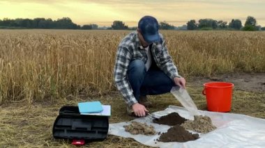 Professional farmer filling sample bag with soil, preparing material for laboratory analysis, working at field at dawn. Agronomist conducting sampling, environment research, soil certification outdoor