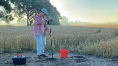 Female agronomist taking sample with soil probe sampler at agricultural grain field at dawn. Woman farmer using drilling tool for soil sampling at morning outdoors. Environmental protection, research