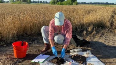 Female agronomist in rubber gloves sampling soil by taking sample into test tube for laboratory analysis outdoors. Scientist preparing material for research. Environment protection, soil certification