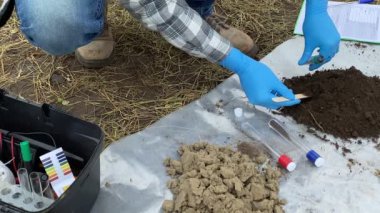 Closeup of male specialist hand in protective gloves taking soil sample into test tube, preparing material for laboratory analysis outdoors. Agronomist working at field. Environment research
