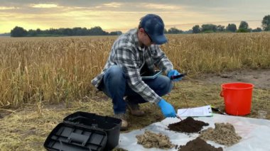 Male agronomy specialist measuring soil pH value, acidity, temperature, moisture by using soil tester, entering data to digital tablet outdoors. Professional farmer performing certification of soil