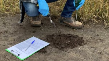 Low section professional farmer measuring soil temperature, pH value, moisture by using soil tester, making records in sample information sheet at agricultural field at morning. Soil certification