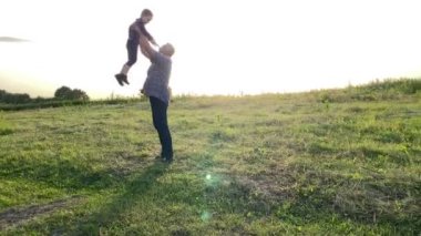 Silhouette of man throwing little boy high in gold lights of summer sun at meadow. Father and son spending time together rejoicing togetherness while leisure time at nature. Happiness in simple living