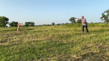 Experienced father teaching daughter to fly kite at sunset outdoors. Little girl helping grandpa to fly kite at meadow. Family with one child spending time together, rejoicing playtime at nature.