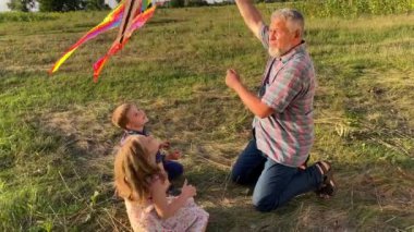 Charming kids with father preparing to fly kite at sunset outdoors. Family with two children spending time together at nature. Grandpa enjoying to have fun with kids at meadow. Happiness simple living