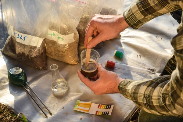 Closeup of male agronomy specialist testing soil sample outdoors, using laboratory equipment, performing soil certification at agricultural grain field sunrise. Environment research soil certification