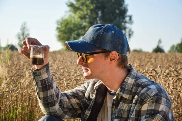 Male agronomy specialist testing soil sample outdoors, using laboratory equipment, performing soil certification at agricultural grain field sunrise. Environment research, soil certification