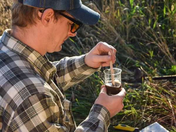 Male agronomy specialist testing soil sample outdoors, using laboratory equipment, performing soil certification at agricultural grain field sunrise. Environment research, soil certification