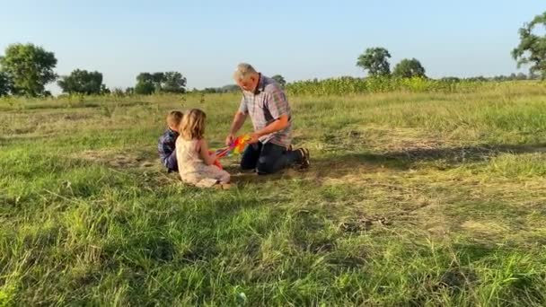 有两个孩子的家庭日落时在农村度过闲暇时光 照顾爷爷教孩子 准备放风筝到农村去 可爱的孩子们在户外学习放风筝 移动射击 — 图库视频影像