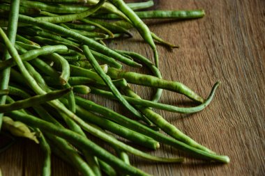 Çiğ, yeşil kuşkonmaz fasulye, ahşap masa. Durgun yeşil sebze gün ışığını aydınlattı. Hasat konsepti. Organik gıda deseni. Vejetaryen yemeği. Sağlıklı beslenme. Yemek pişirmek için gerekli malzemeler
