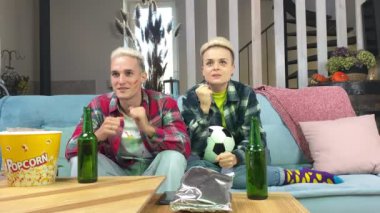 Kapalı mekanda canlı futbol maçı izleyen ve yüzünde İspanyol bayrağı olan genç bir futbol taraftarı. Şık bir kadın ve mutlu bir adam kutlama yapmak için evde koltukta oturuyor.