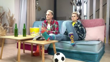 Canlı spor müsabakalarını izleyen neşeli futbol taraftarı çift içeride koltukta oturuyor. Mutlu adam ve stil sahibi genç kadın gülüyorlar evde futbol takımına tezahürat yaparak eğleniyorlar.