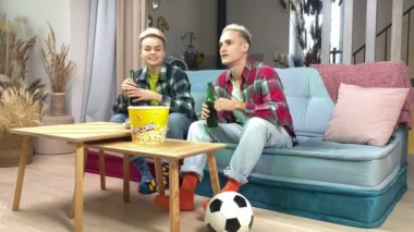 Heteroseksüel çift TV 'de canlı futbol maçı izliyor, spor takımına tezahürat yapıyor, bira içiyor, evde kanepede oturuyor. Kısa saçlı şık genç bir kadın evde futbol hayranıyla eğleniyor.