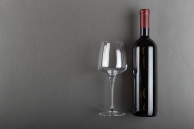 Mantarlı kırmızı şarap şişesi ve gri arka planda boş şarap kadehi. Alkolik içki. Şarap yapma konsepti. Mesaj için yer var. Üst görünüm.