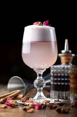Bardakta köpük olan pembe kadın kokteyli. Kurumuş gülle süslenmiş. Arka planda görünen barmen envanteri var.