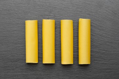 Çiğ cannelloni makarnası, genellikle et veya sebzelerle doldurulmuş siyah bir arka planda bulunan boru şeklinde bir makarna. İtalyan kanelloni makarna tüpleri. Üst görünüm.