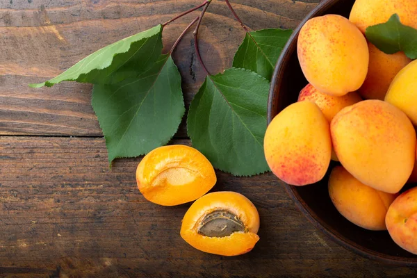 Olgun kayısılar ve kayısı yaprakları ahşap bir masada bir kasede. Ev bahçesinden taze meyve. Sağlıklı yemek..