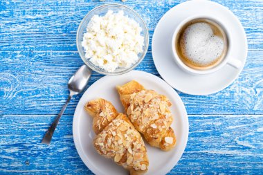 Taze Fransız kruvasanı, süzme peynir ve mavi ahşap masada kahve ile nefis bir kahvaltı. Mesaj için yer var. Üst görünüm.