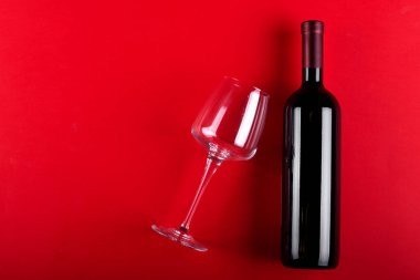 Kırmızı şarap şişesi ve boş şarap kadehi. Kırmızı arka planda. Romantik bir ruh hali. Mesaj için yer var. Üst görünüm.