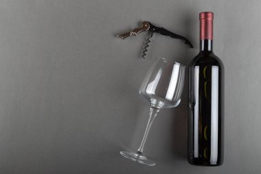 Mantarlı kırmızı şarap şişesi, tirbuşon ve gri arka planda boş şarap kadehi. Alkolik içki. Şarap yapma konsepti. Mesaj için yer var. Üst görünüm.