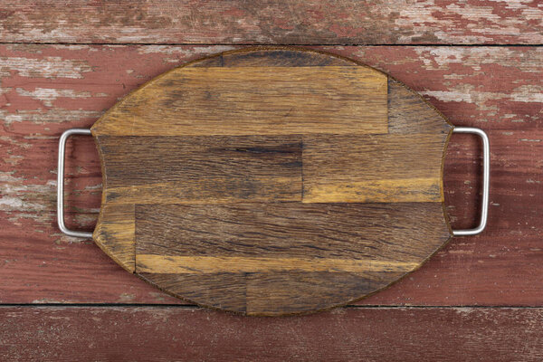 Empty oval cutting board with iron handles on a red wooden table. Top view.