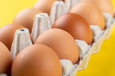 Sarı arka planda yumurta kabında tavuk kahverengi çiğ yumurta. Yemek yapmak için gerekli malzemeler. Sağlıklı beslenme bir kavramdır. Yatay yönelim, seçici odak.