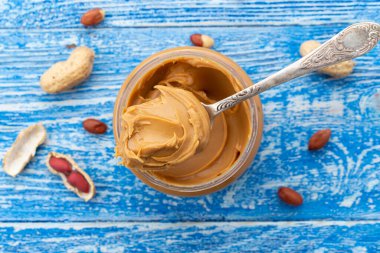 Açık kavanozdaki fıstık ezmesi ve derisindeki fıstıklar mavi masaya saçılmış. Mesaj için yer var. Yakın çekim..