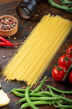 Taze domatesli çiğ makarna, biber, kuşkonmaz fasulyesi, baharat ve peynir ahşap bir masada. İtalyan spagettisi için yemek malzemeleri..