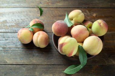 Tahta bir masada, kil bir kasede yapraklarla olgunlaşmış şeftaliler. Taze hasat.