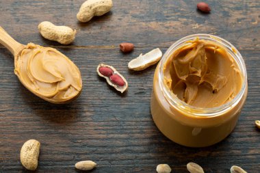 Ahşap kaşık, fıstık ezmesi kavanozu ve eski bir arka planda dağınık fındık..