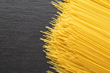 Siyah tahtada sarı uzun spagetti. Sıraya dizilmiş ince makarna. Sarı İtalyan makarnası. Uzun spagetti. Çiğ spagetti duvar kağıdı. İnce spagetti. Yemek geçmişi konsepti. Metin için boşluk.