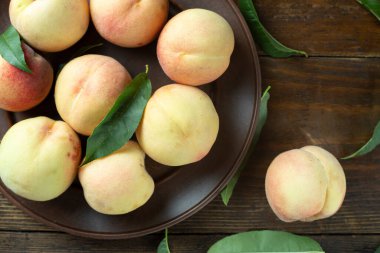 Tahta bir masada, kil bir tabakta yapraklarla olgunlaşmış şeftaliler. Taze hasat. Üst görünüm.