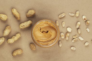 Kağıt masadaki kavanozda kremalı ve pürüzsüz fıstık ezmesi. Doğal beslenme ve organik gıda. Üst görünüm.